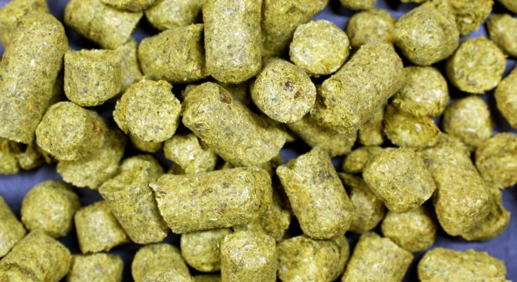 A close-up view of cylindrical, greenish-brown pellets, likely to be animal feed or pet food, filling the frame HBC 472 Hops